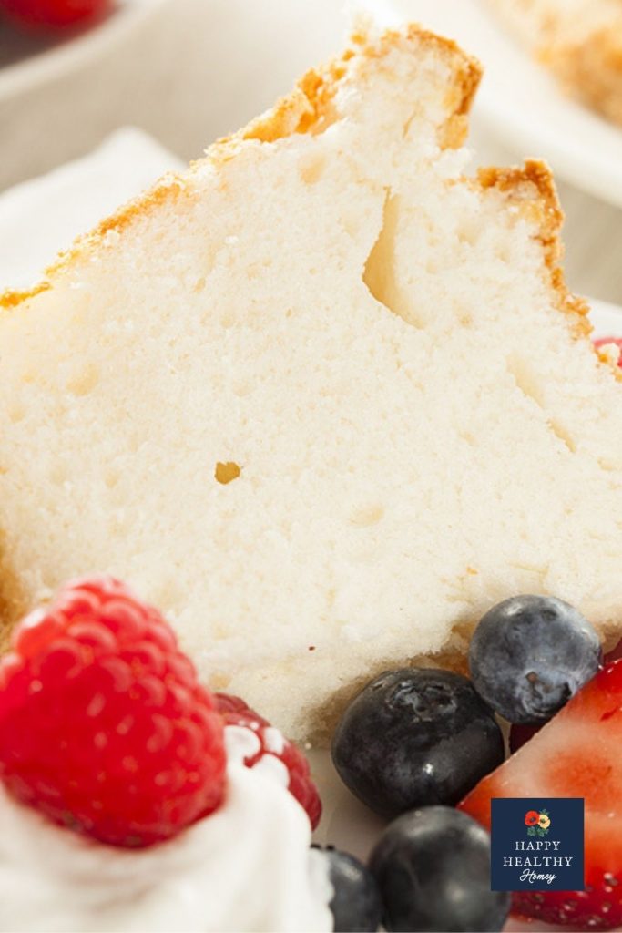 Slice of angel food cake with fresh blueberries and strawberries on a white plate.