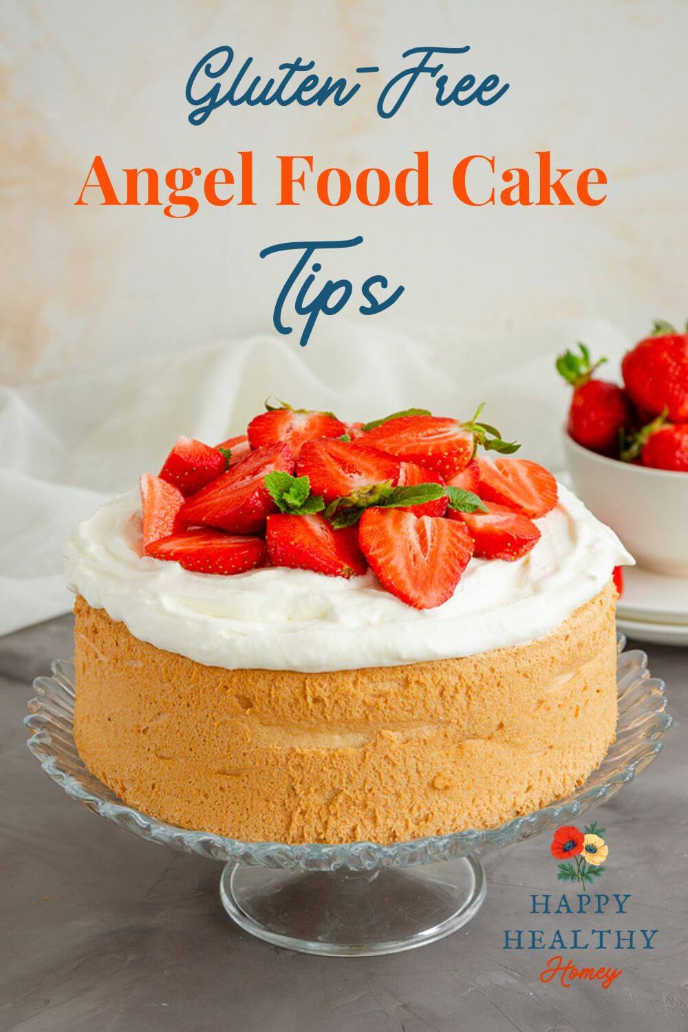 Gluten-free angel food cake topped with whipped cream and fresh strawberries on a glass cake stand.