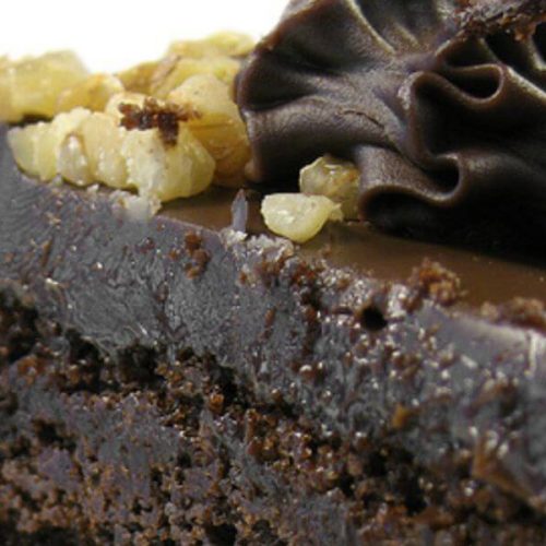 Moist chocolate cake slice topped with glossy dark chocolate frosting and chopped walnuts, showing the rich texture and creamy finish