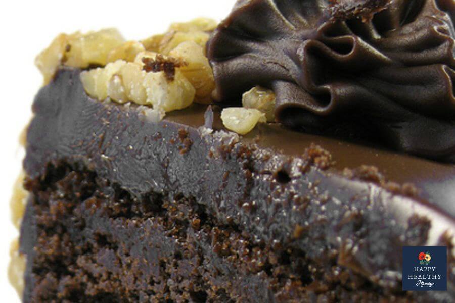 Moist chocolate cake slice topped with glossy dark chocolate frosting and chopped walnuts, showing the rich texture and creamy finish