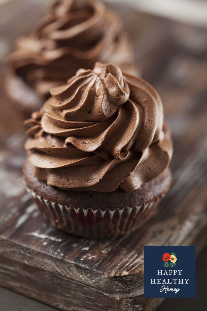Detailed view of a chocolate cupcake with thick, swirled dark chocolate frosting on a wooden table, emphasizing texture and richness.