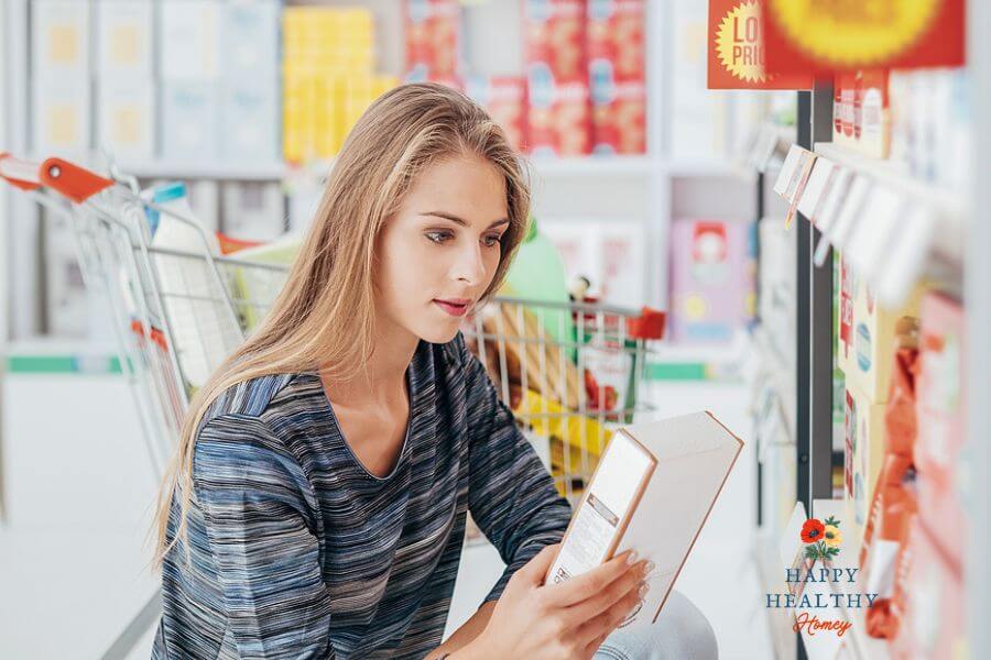 Young woman kneeling in a grocery store aisle, reading the back of a product box. The image is used to promote a blog post on how to read food labels for gluten-free living.