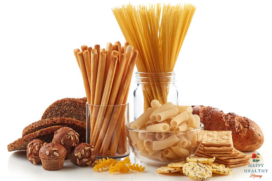 Variety of gluten-based foods like pasta, breadsticks, loaves, muffins, and crackers on a white background, emphasizing common sources of gluten in the kitchen.