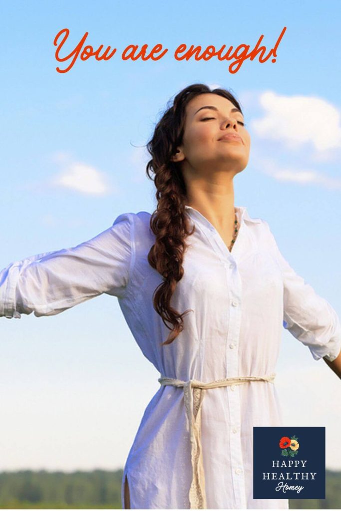 Peaceful woman in a white dress standing outdoors with eyes closed and arms outstretched under a blue sky, symbolizing freedom, self-worth, and inner peace.