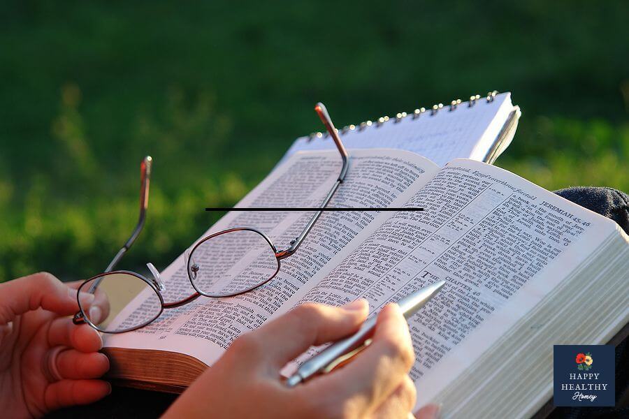 Close-up of an open Bible with reading glasses and a pen resting on the pages, held by someone studying Scripture outdoors, representing reflection, faith, and personal growth through God's Word.