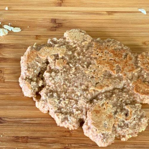 Flatbread made from oats on a wooden board with scattered rolled oats, naturally gluten-free and flourless.