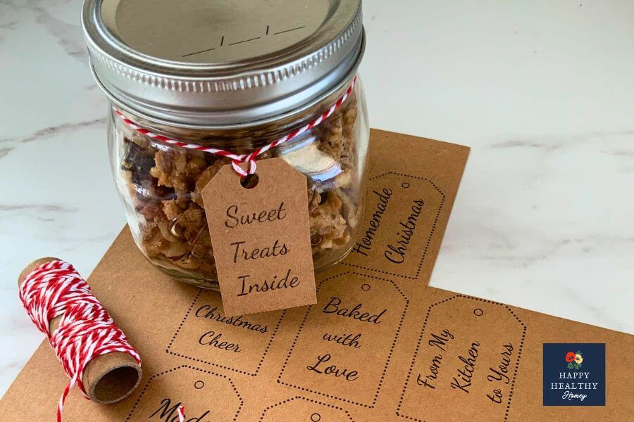 Jar of candied walnuts tied with red baker’s twine, sitting on printable Christmas gift tags with a roll of twine beside it.