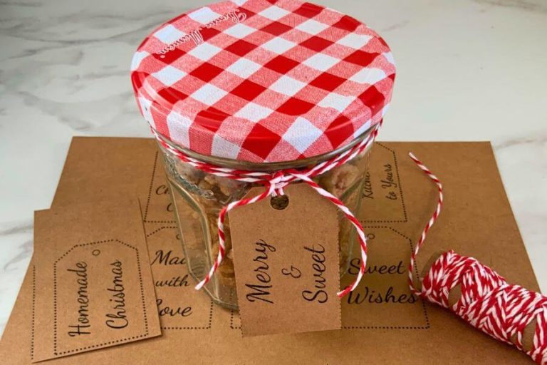 Small jar of homemade candied walnuts with a red gingham lid, twine, and kraft gift tag on top of printable Christmas gift tags.