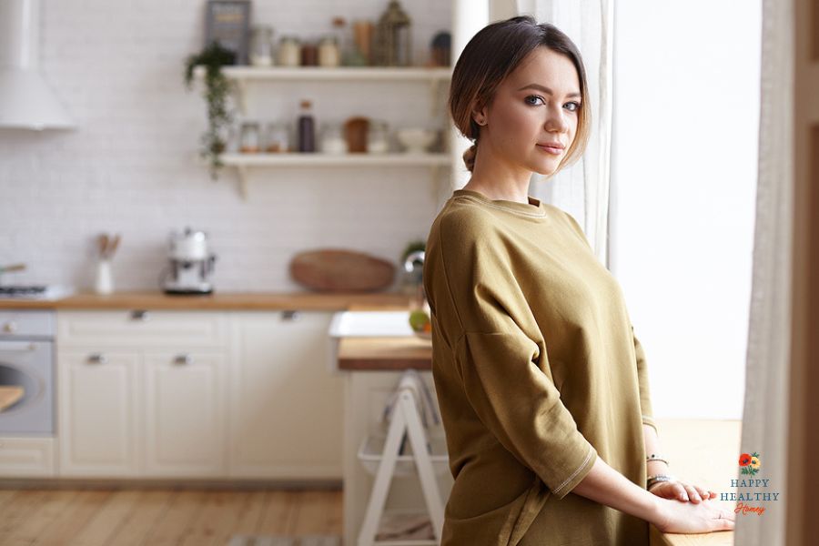 Woman in kitchen standing in front of a window looking peaceful.