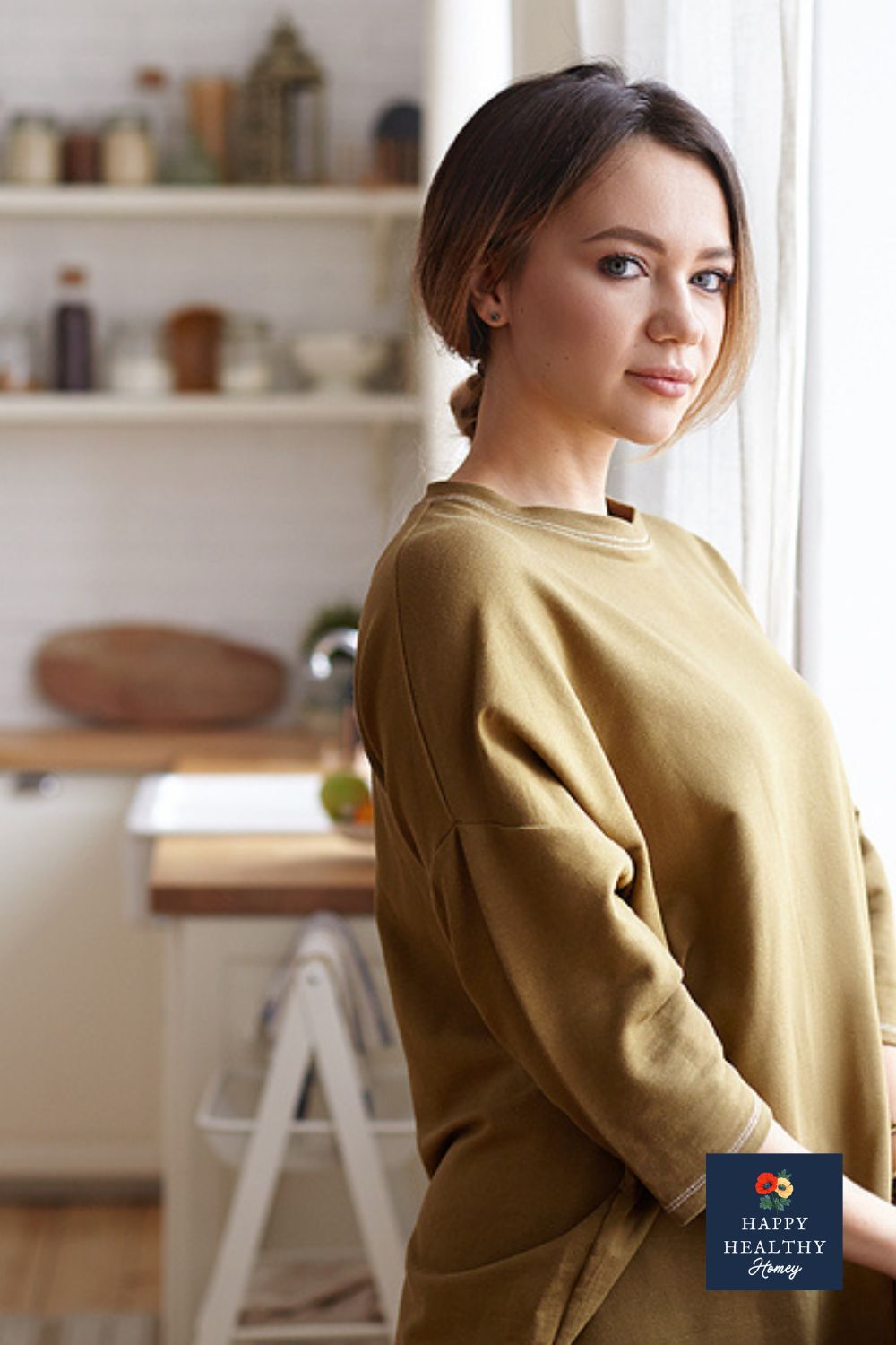 Young woman standing in kitchen in front of a window looking peaceful.