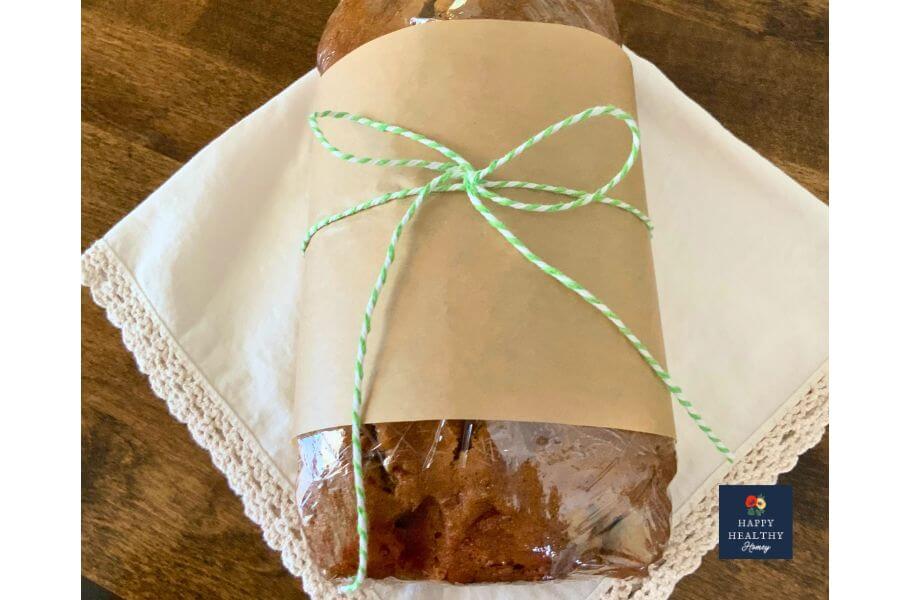 Loaf of gluten-free Zucchini Bread wrapped in parchment paper and tied with green and white kitchen string, sitting on a cloth napkin.