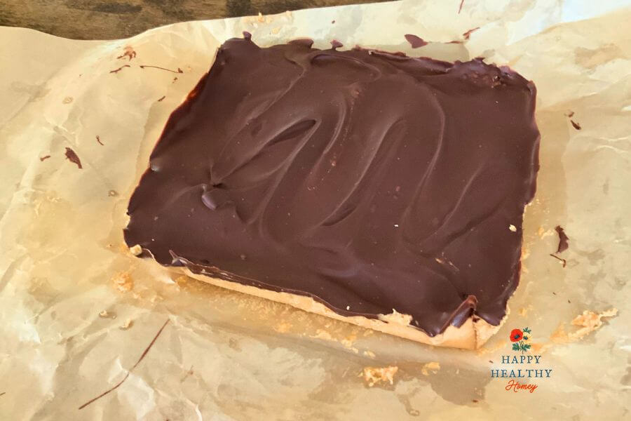 Gluten-free no-bake chocolate peanut butter bars topped with smooth chocolate on parchment paper.

