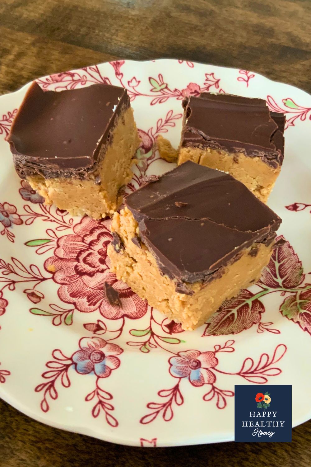 Three gluten-free no-bake chocolate peanut butter bars with a creamy peanut butter filling and smooth chocolate topping on a floral plate.